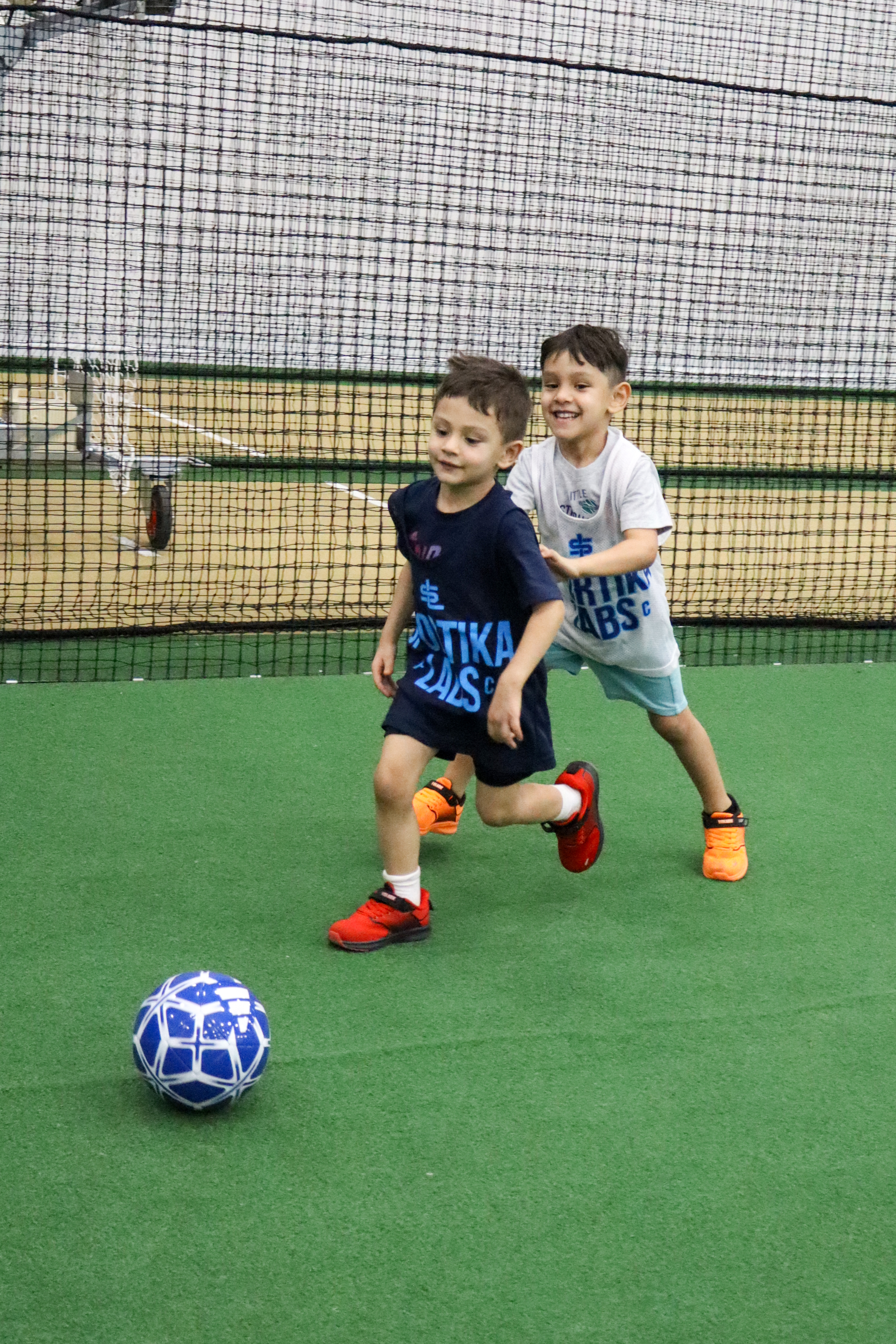 Two young players chasing a soccer ball, smiling and running together