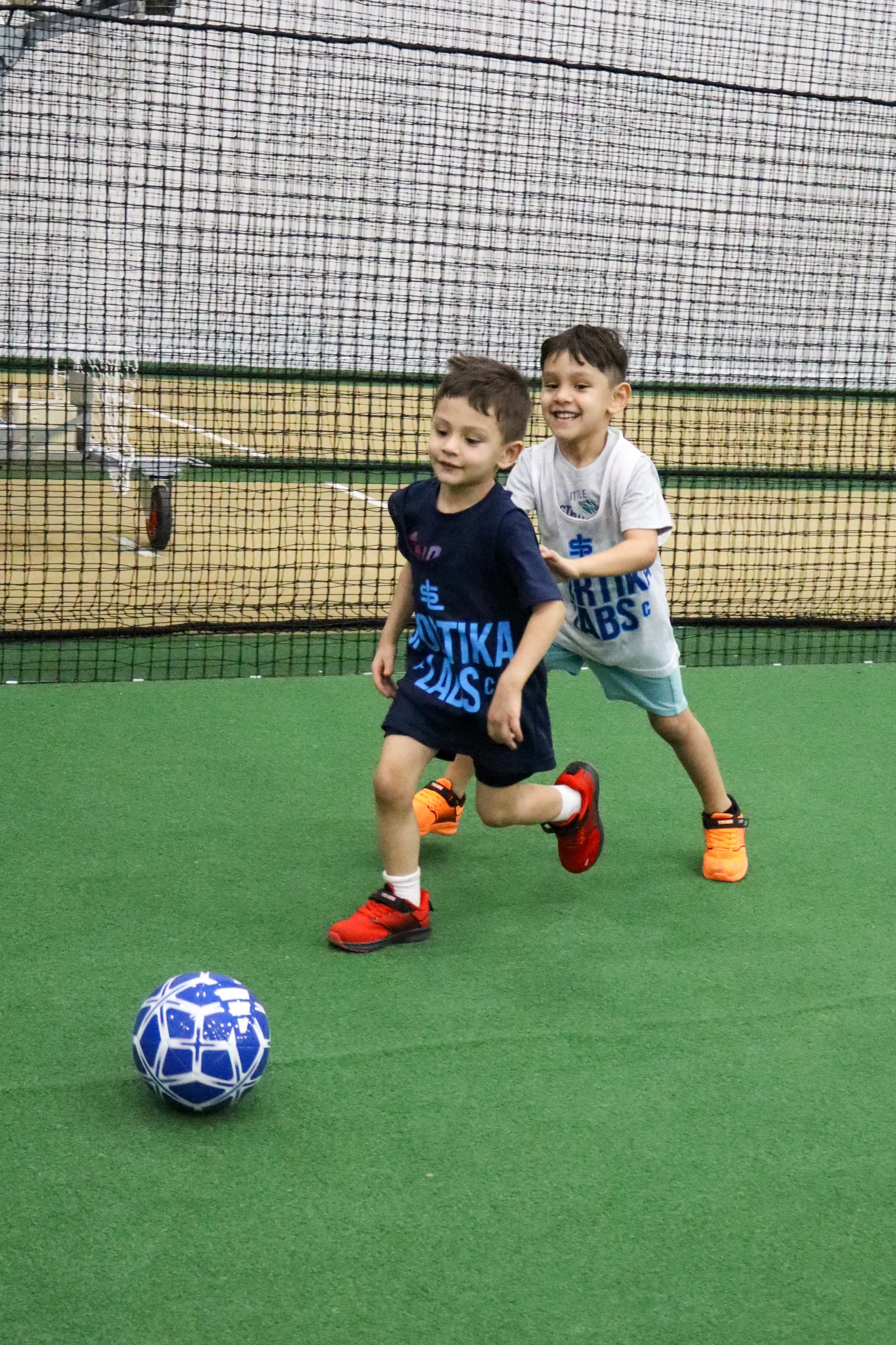 Two young players chasing a soccer ball, smiling and running together