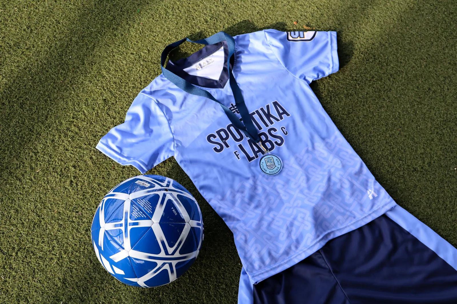 Sportika Labs jersey, shorts, ball, and trial-day medal on turf